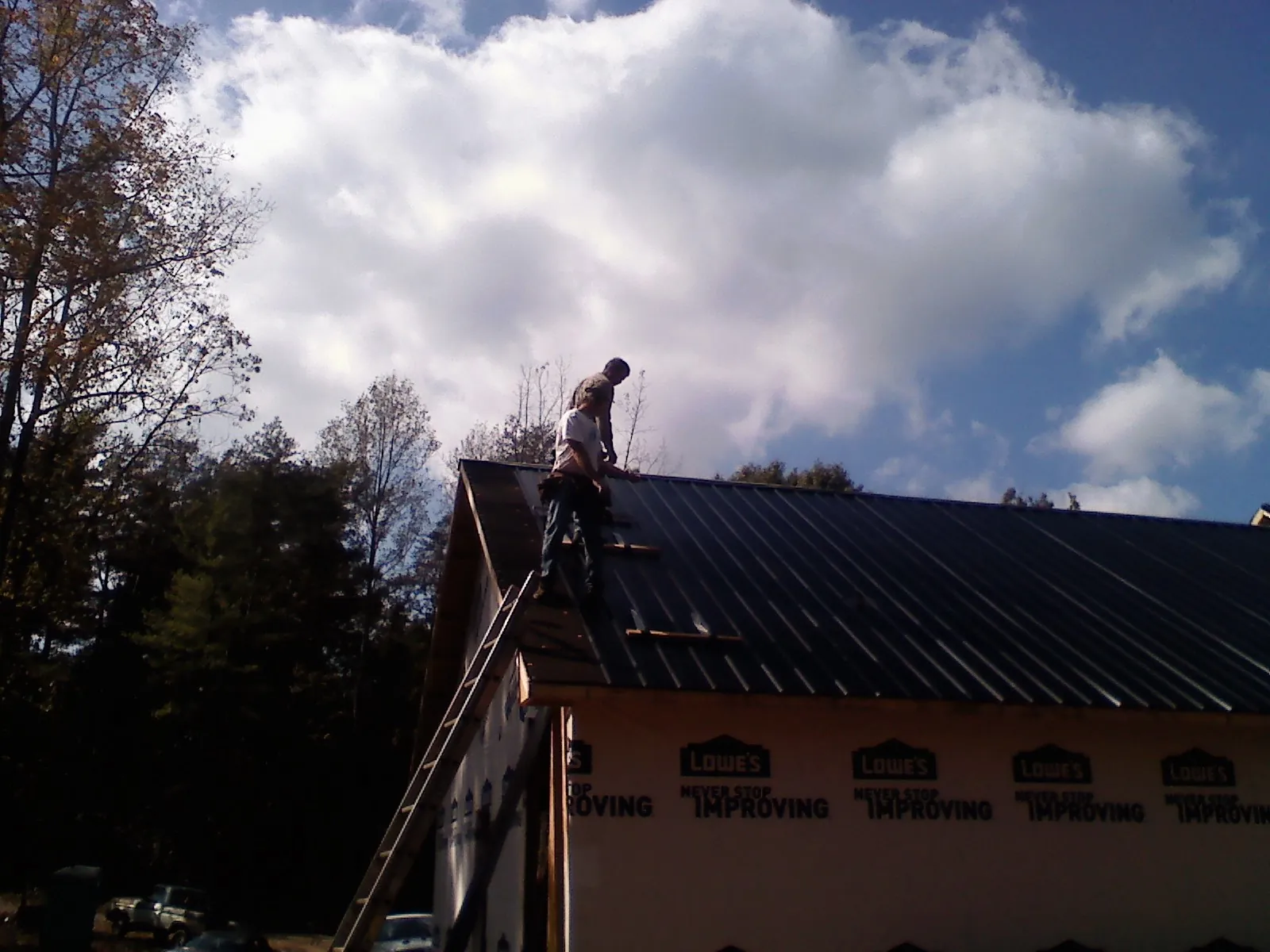Roofer fastening dark metal panels high against a cloudy sky, from a Roof Inspection job in Piedmont