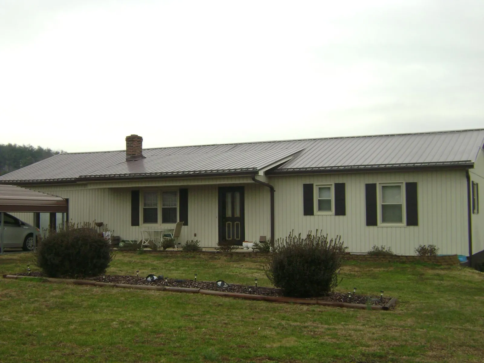 Brown metal roof on a cream sided ranch home with a brick chimney in Piedmont